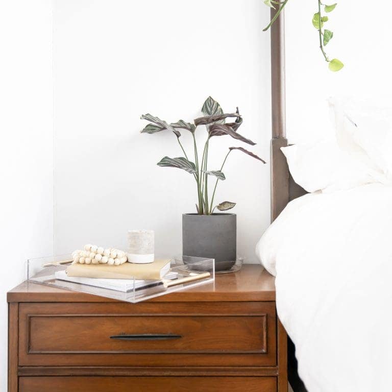 Wood nightstand by bed with plant