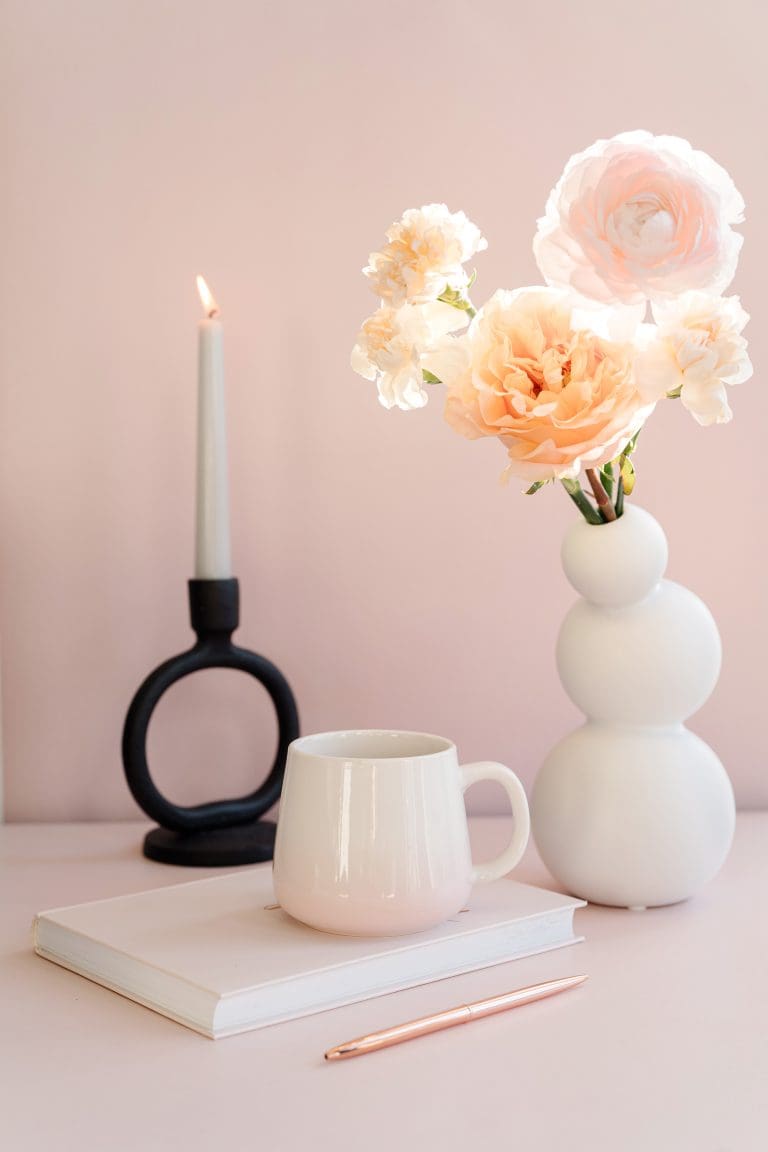 Flowers in a vase, candle and cup of tea atop a notebook